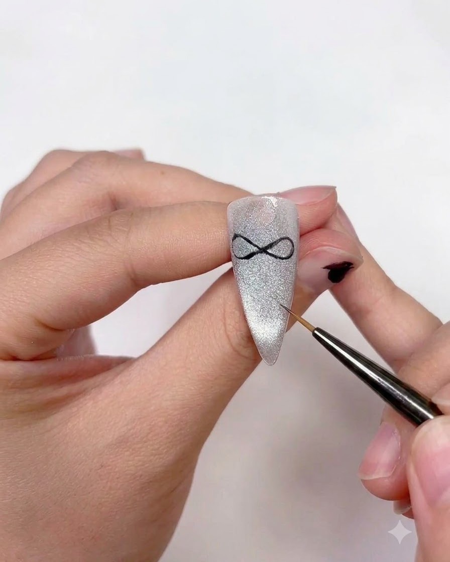 Una artista de uñas usando un pincel delineador fino para añadir dos colas de cinta curvas que se extienden hacia abajo desde el centro del arte del lazo.