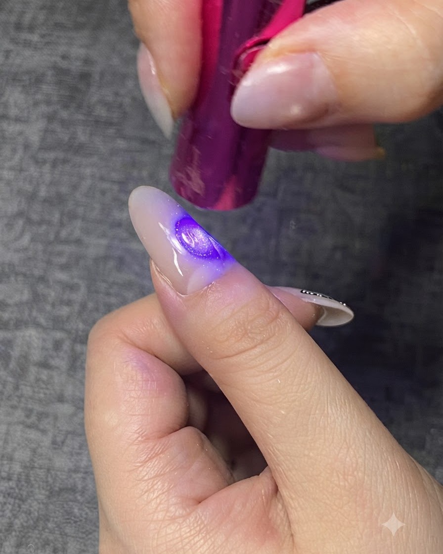 Una mini lámpara UV/LED curando una capa de gel transparente en una uña.