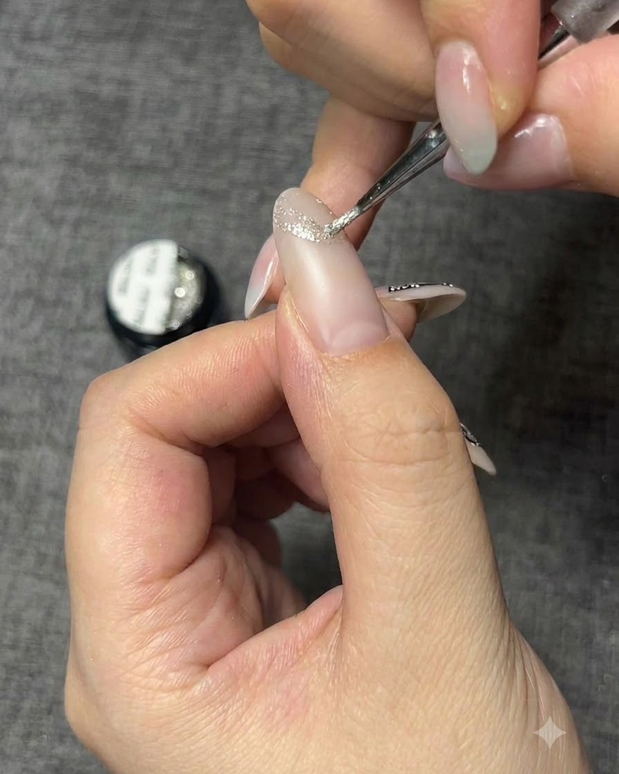 Un pincel de detalle aplicando gel con brillo plateado para crear la silueta de una mariposa.