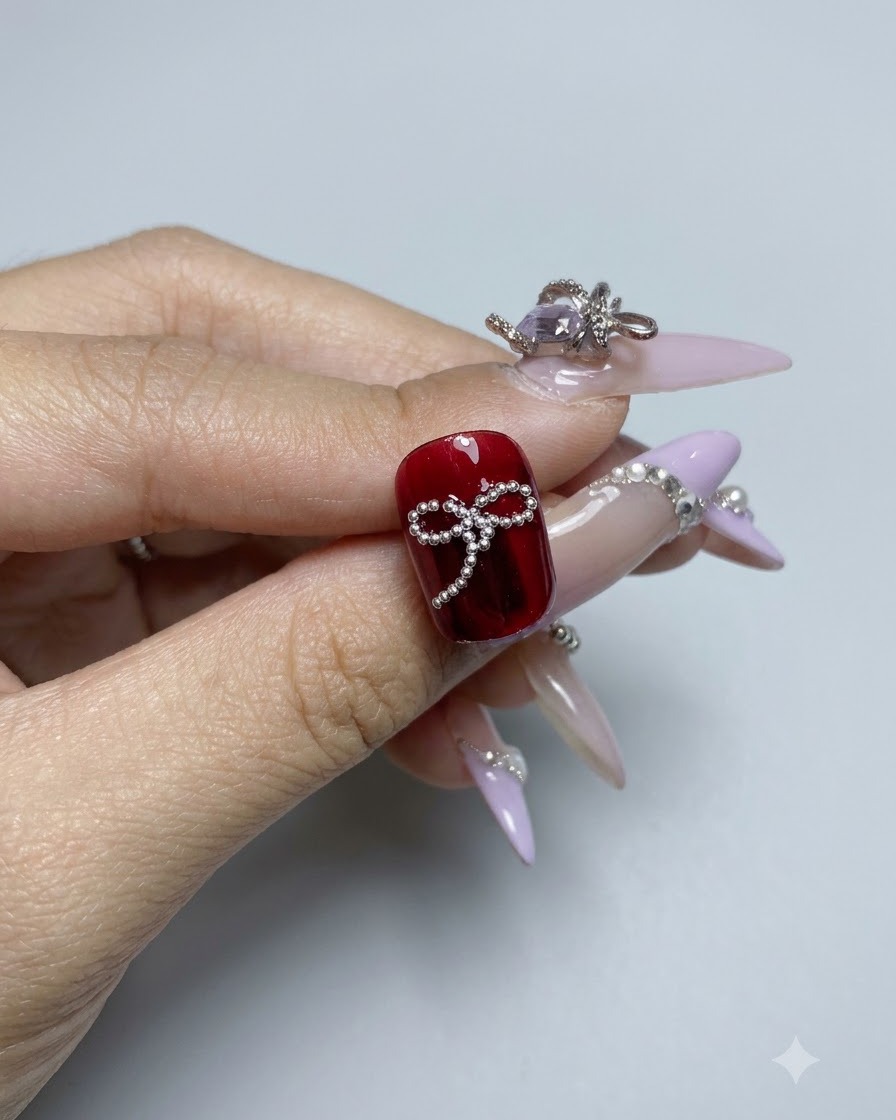 Un diseño completado de lazo con cuentas de acero sobre la superficie de una uña de gel rojo brillante vista de cerca.