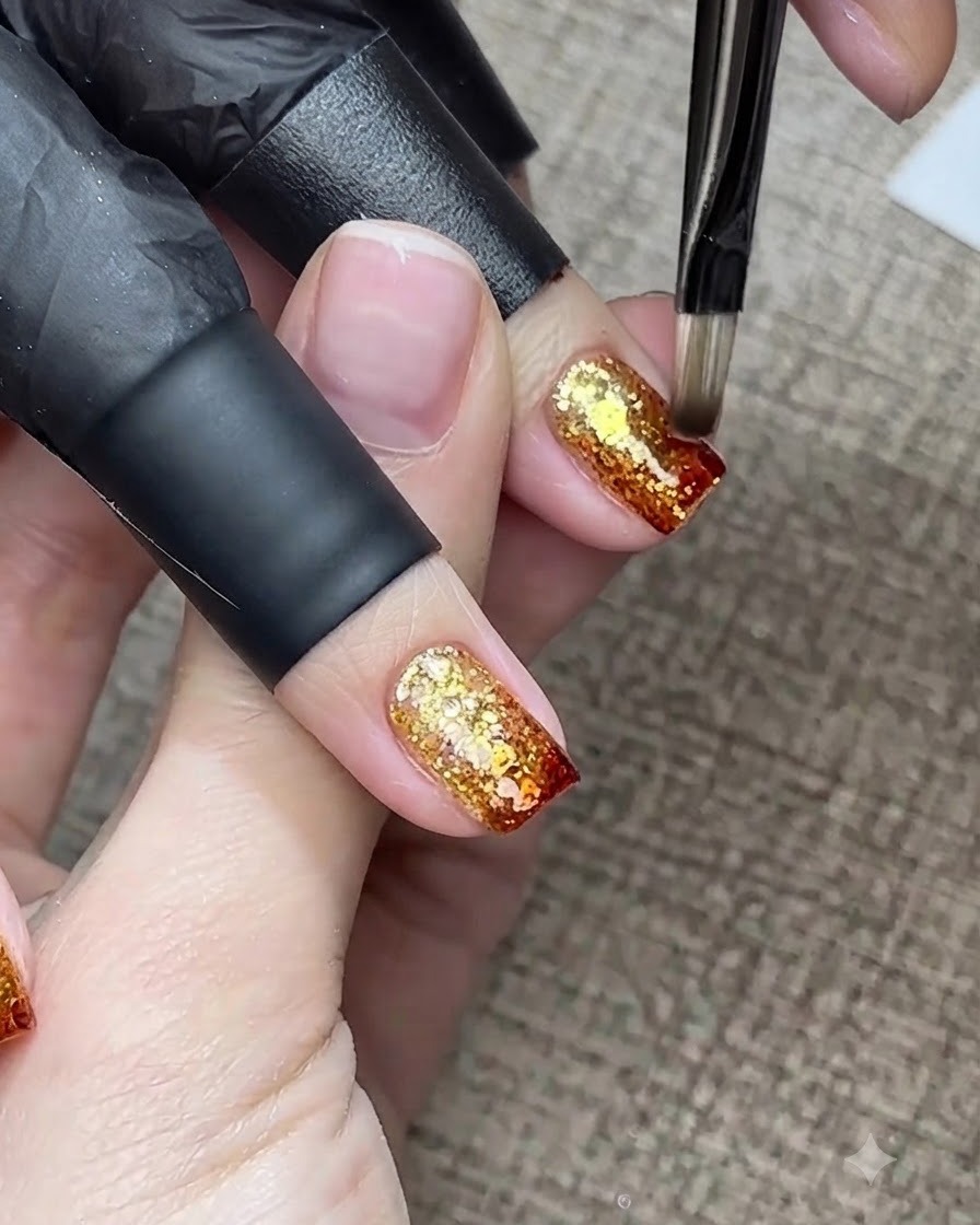 Un pincel fino de nail art aplicando mediante toquecitos gel ámbar rojo-marrón más oscuro en el borde extremo de la uña.