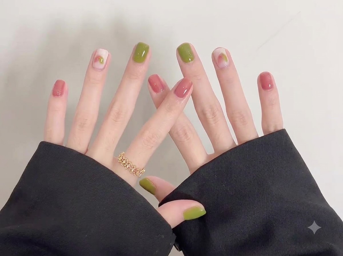 Un plano detalle de cerca enfocado en las uñas brillantes verdes y rosas de la mano derecha con delicado arte doodle.