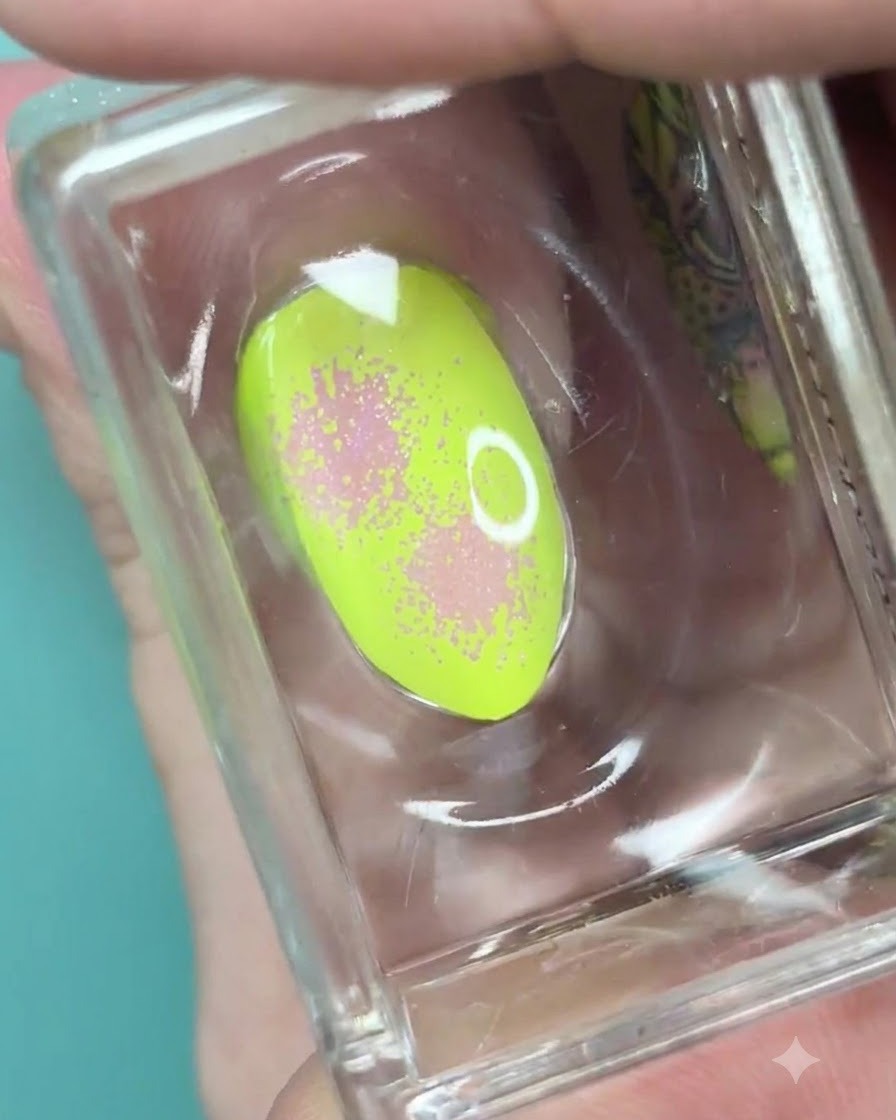 Un sello de silicona transparente que sostiene una uña verde neón con un degradado rosa suave y textura de puntos.