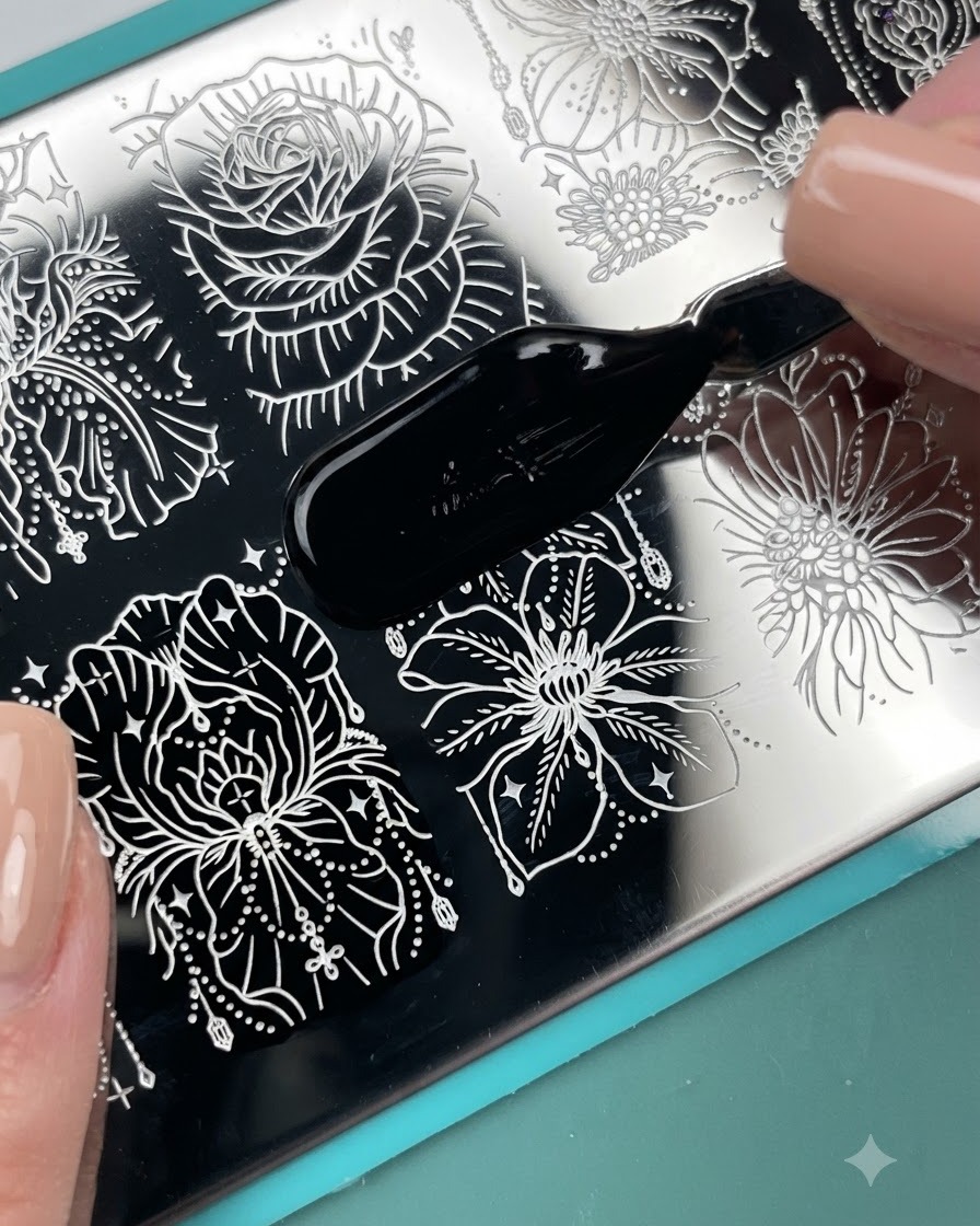 Un aplicador de pincel aplicando esmalte de estampado negro a través de un patrón floral grabado en una placa de metal para estampar.
