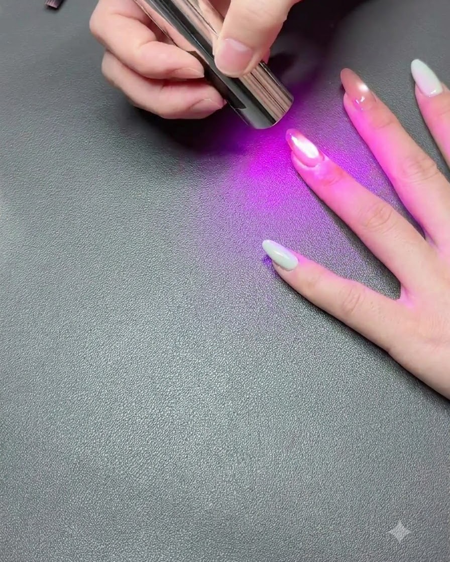Una mano descansando sobre una superficie oscura mientras una lámpara UV portátil cura el esmalte de gel de ojo de gato.