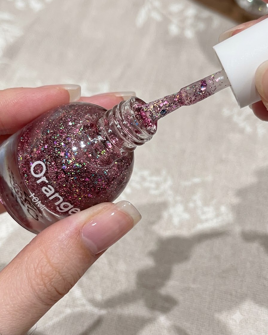 Un pincel aplicando una capa delgada de gel de purpurina rosa en la mitad superior de una uña natural.