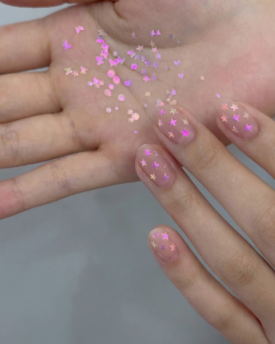 Un pincel de manicura aplicando una capa fina de esmalte en gel nude translúcido sobre una uña natural.