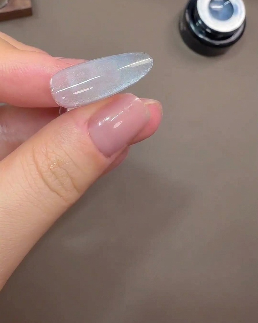 Una uña que muestra un reflejo de luz de ojo de gato ancho sobre un fondo de gel gris-azulado.