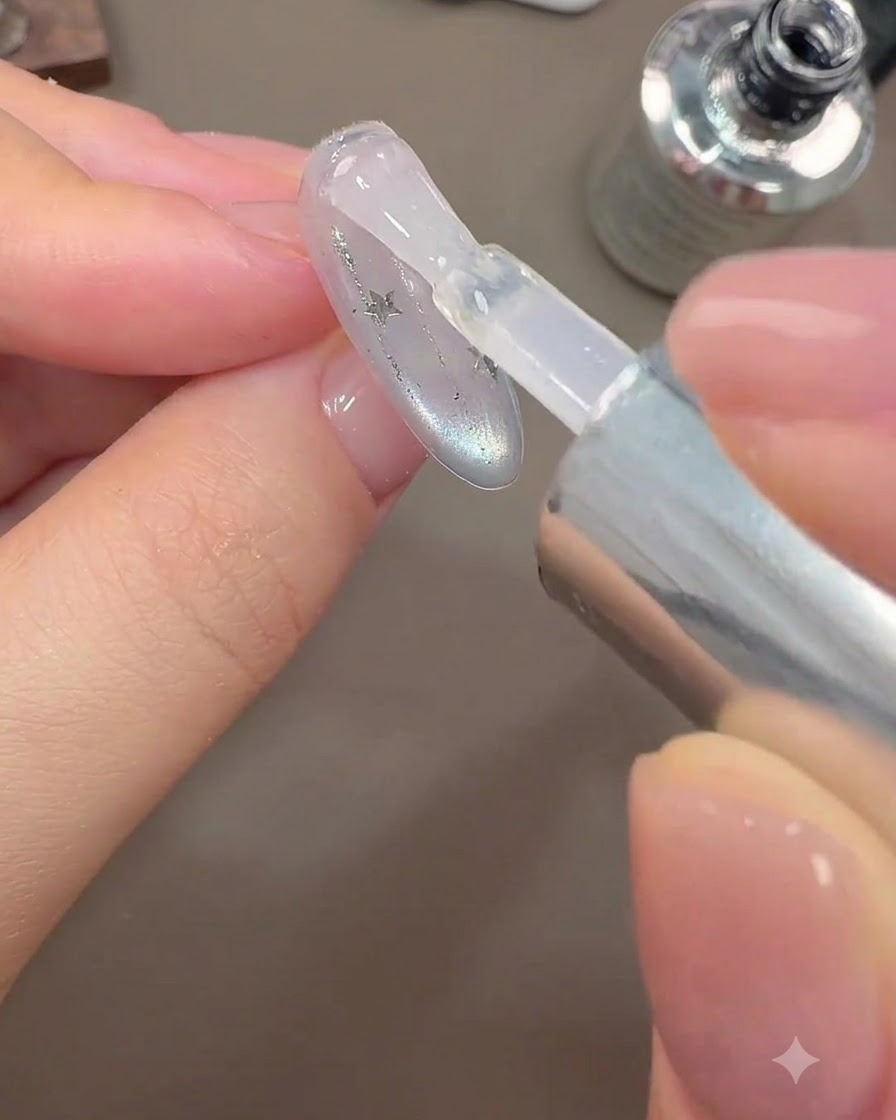 Un pincel aplicando una capa superior brillante final sobre un diseño de uñas galaxy.