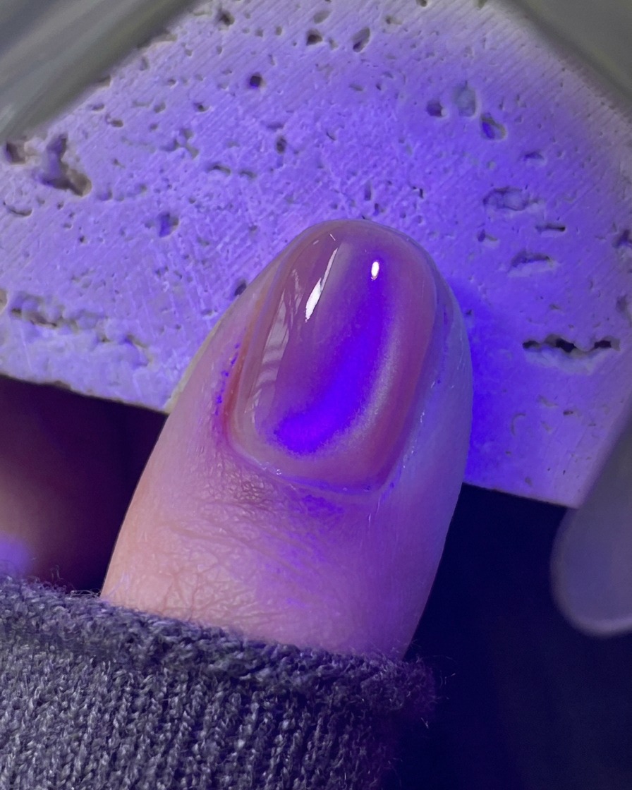 Una uña curándose debajo de una mini lámpara UV/LED morada.