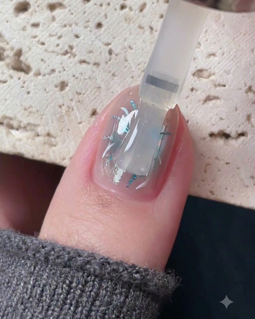 Un pincel aplicando una capa superior transparente autonivelante sobre un diseño detallado de arte de uñas.