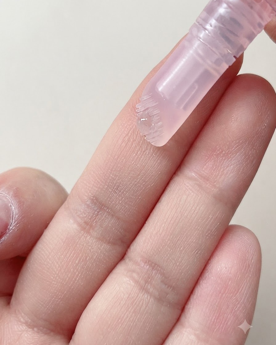 Un cabezal de cepillo suave de un bolígrafo para cutículas dispensando una gota de suero hidratante sobre un dedo.
