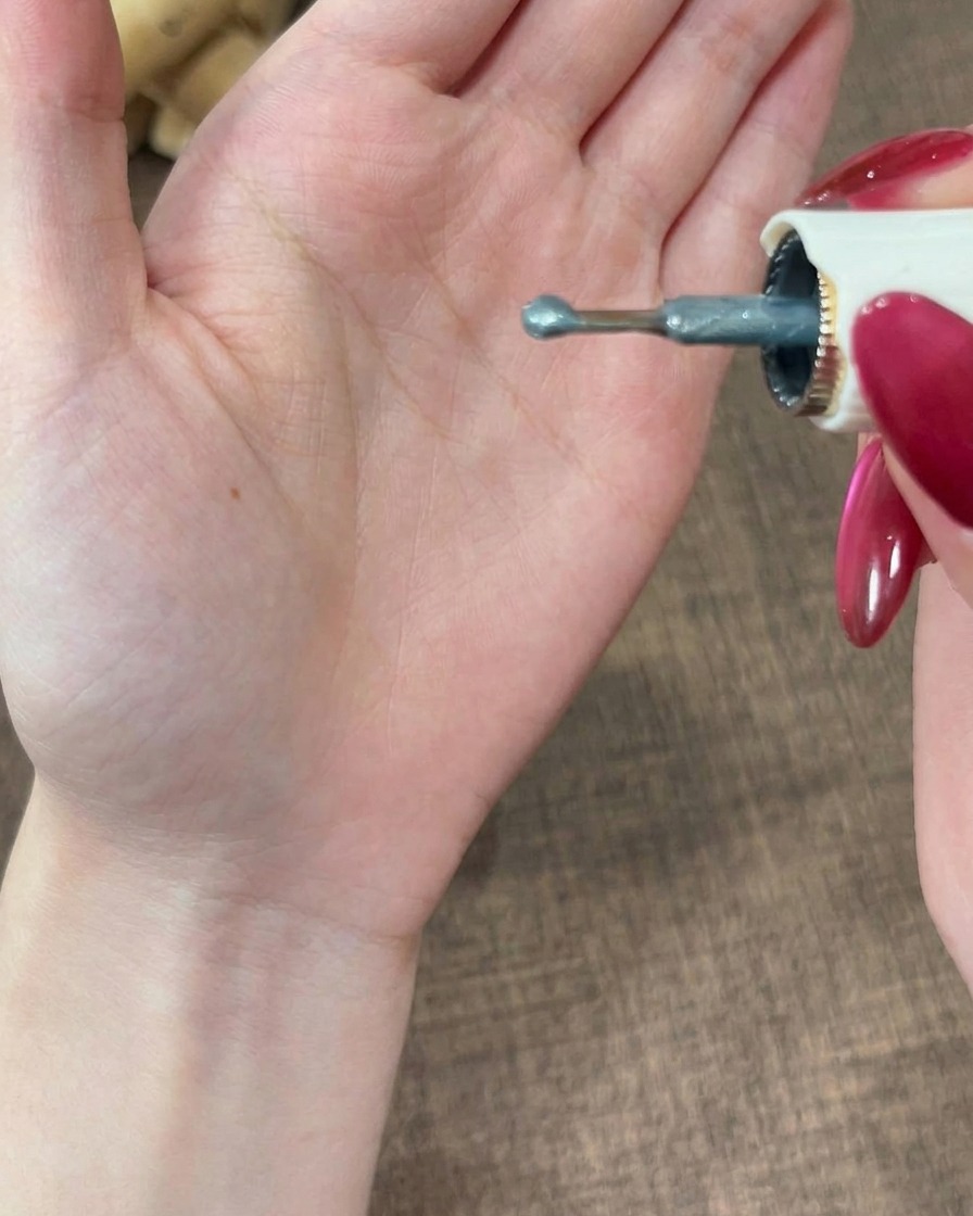 Una vista de primer plano de la punta de un pincel sosteniendo una pequeña gota redondeada de esmalte de gel grisáceo.