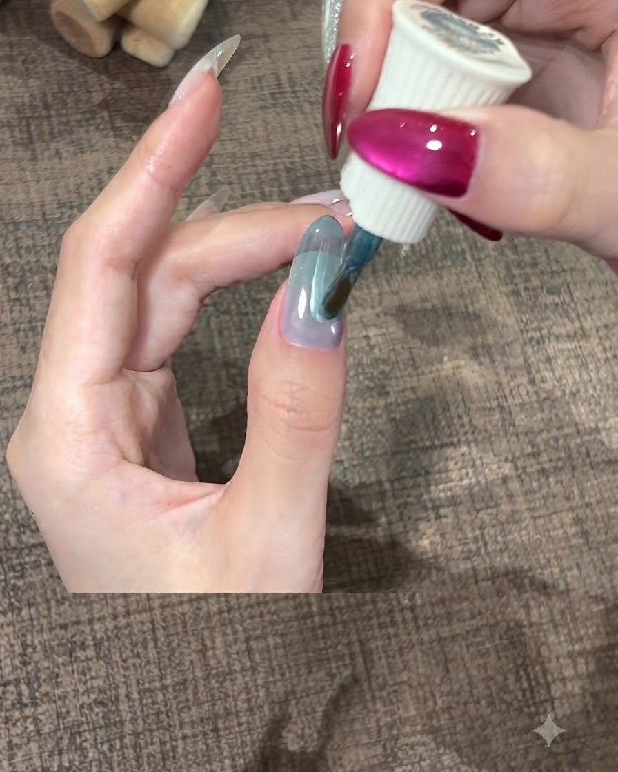 Un pincel esparciendo una capa gruesa de gel verde azulado suavemente sobre la uña del pulgar.