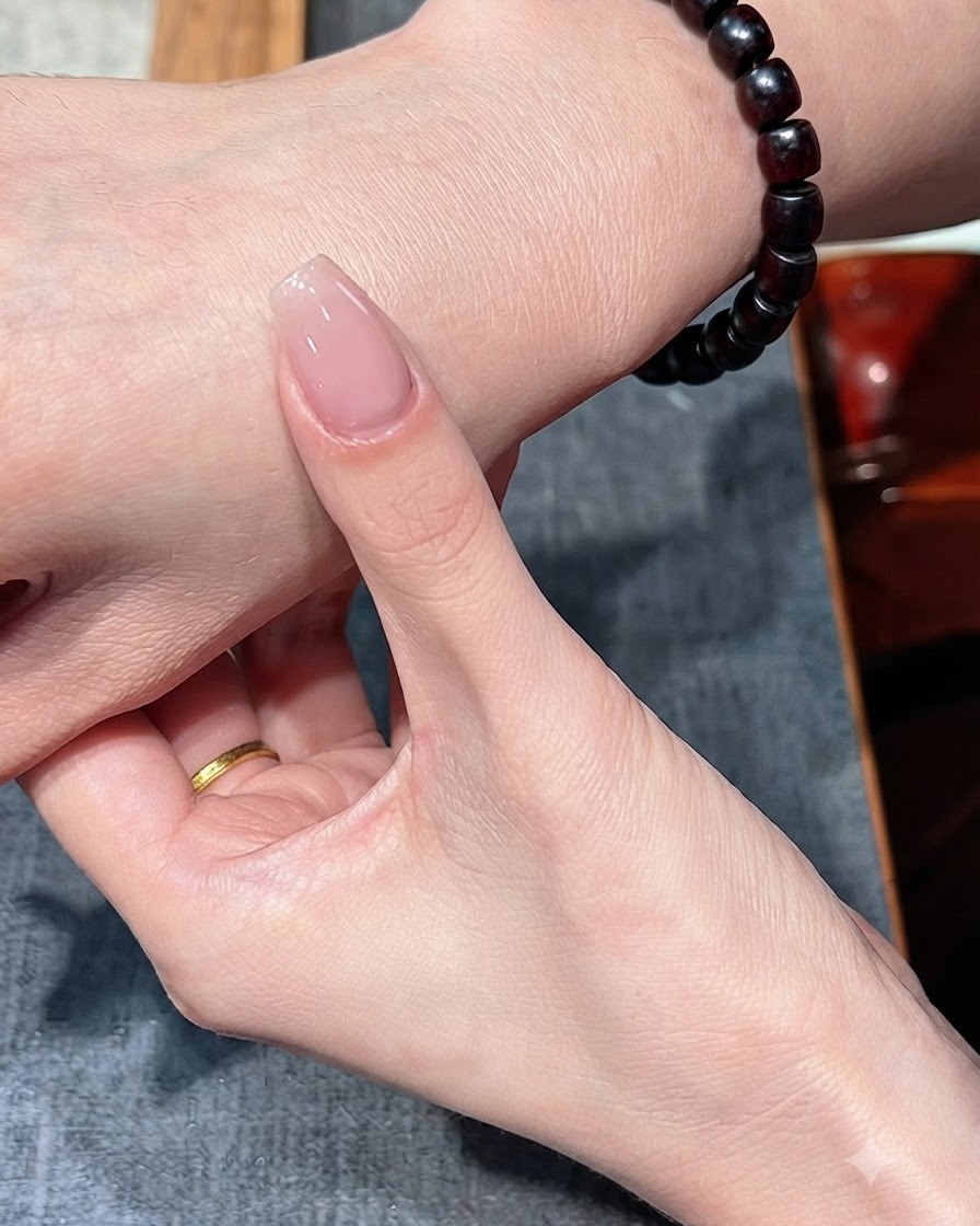 Una uña con una sola capa de esmalte nude sostenida contra el dorso de la mano.