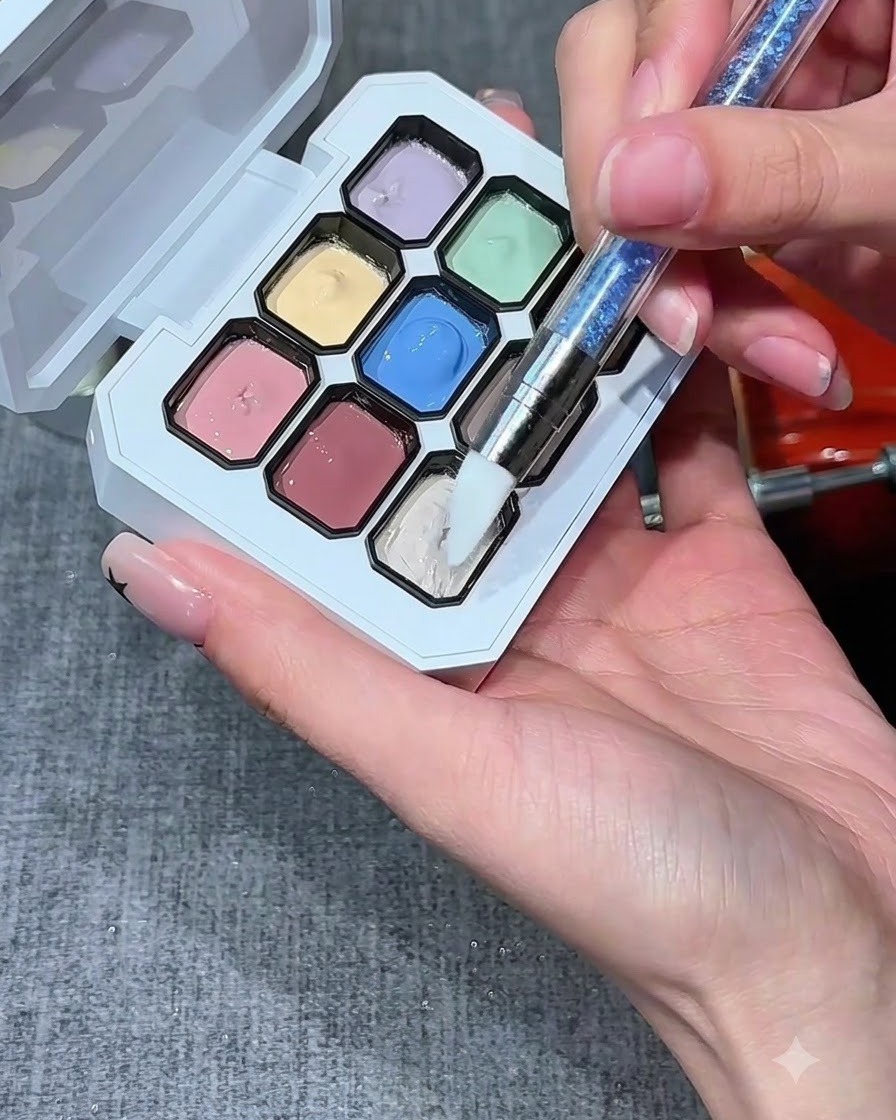 Un pincel de silicona para uñas sumergiéndose en un depósito de gel blanco lechoso sobre una paleta multicolor.