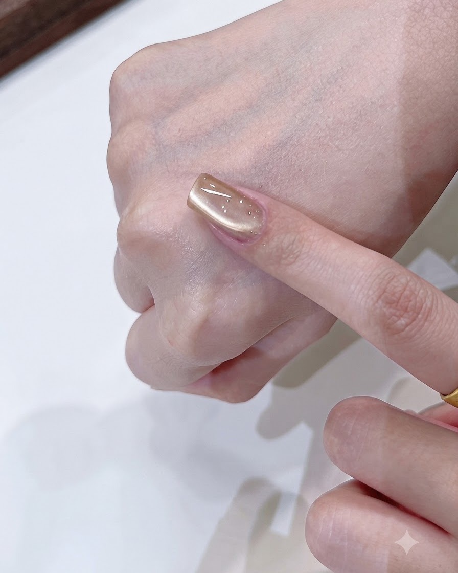 Una herramienta de imán dando forma a una suave reflexión de luz de un solo lado en una uña cat eye de oro champaña.