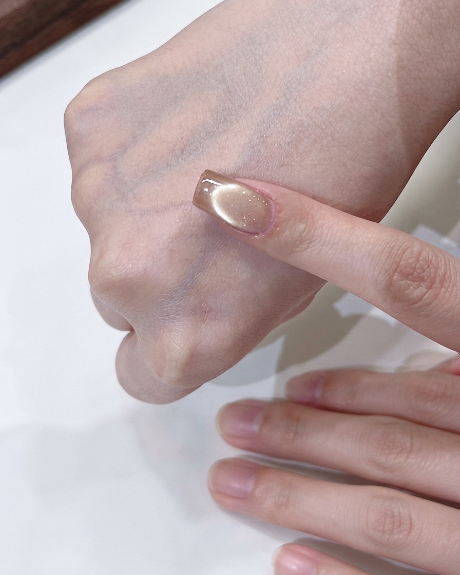 Una mano sosteniendo un imán girando por encima de una uña cat-eye de oro champaña para formar un efecto de luz fluida.