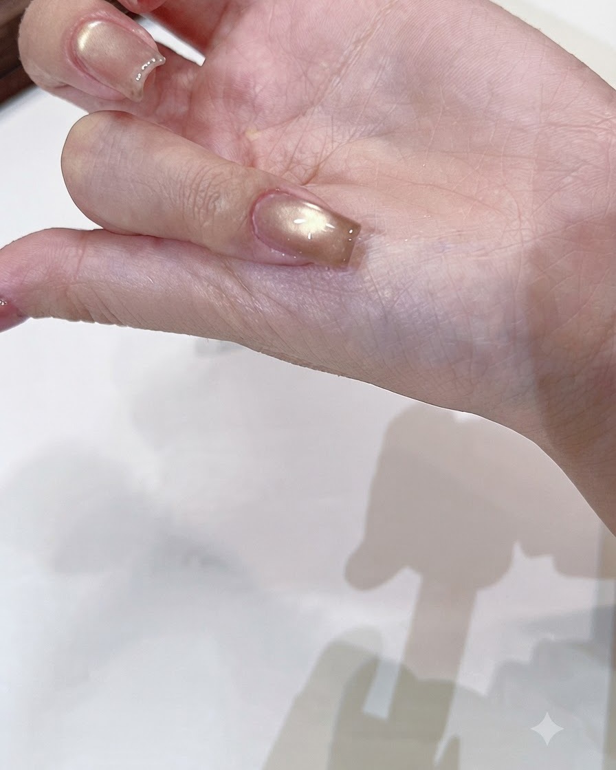 Un pincel aplicando un top coat transparente y brillante sobre una uña cat-eye de oro champaña curada.