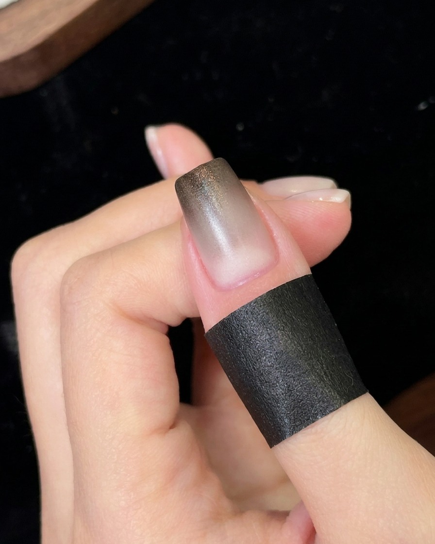 Una uña colocada bajo una pequeña lámpara UV/LED portátil curando la capa de degradado negro recién aplicada.