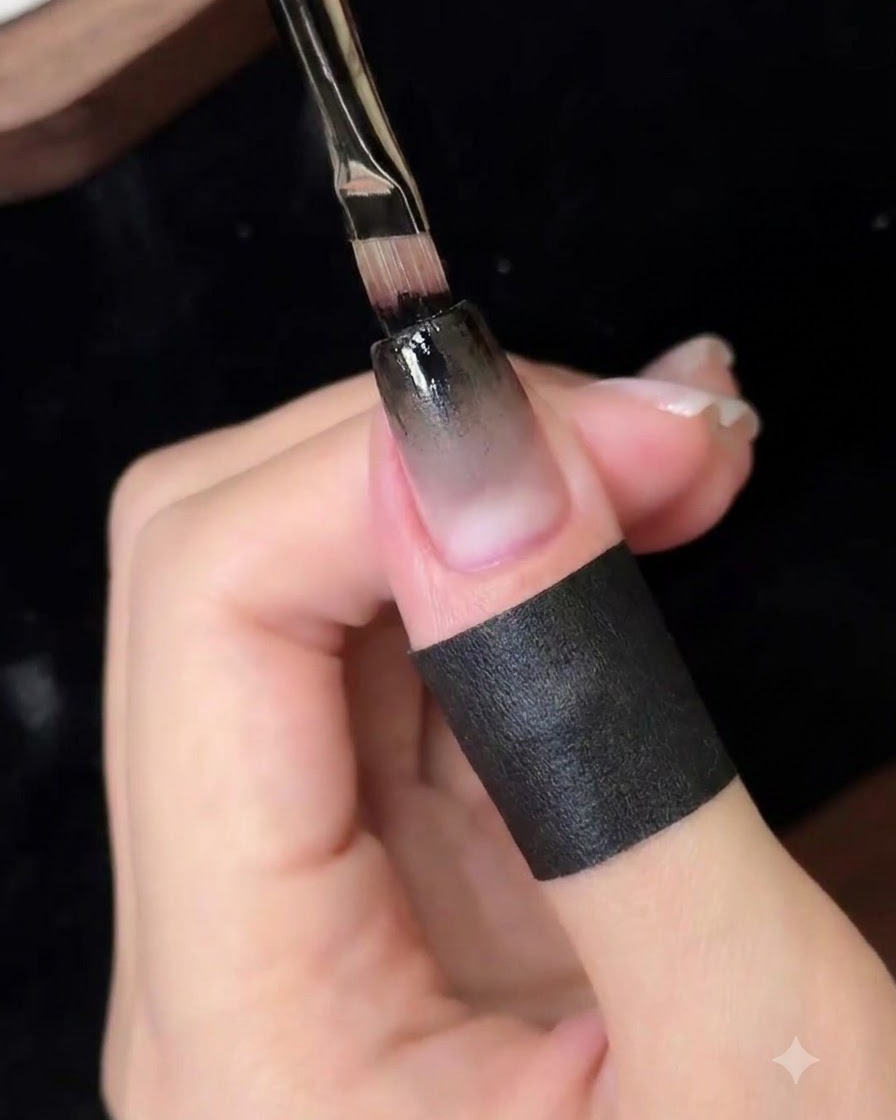 Un pincel de detalle fino aplicando una capa concentrada de gel negro en el borde superior de la uña.