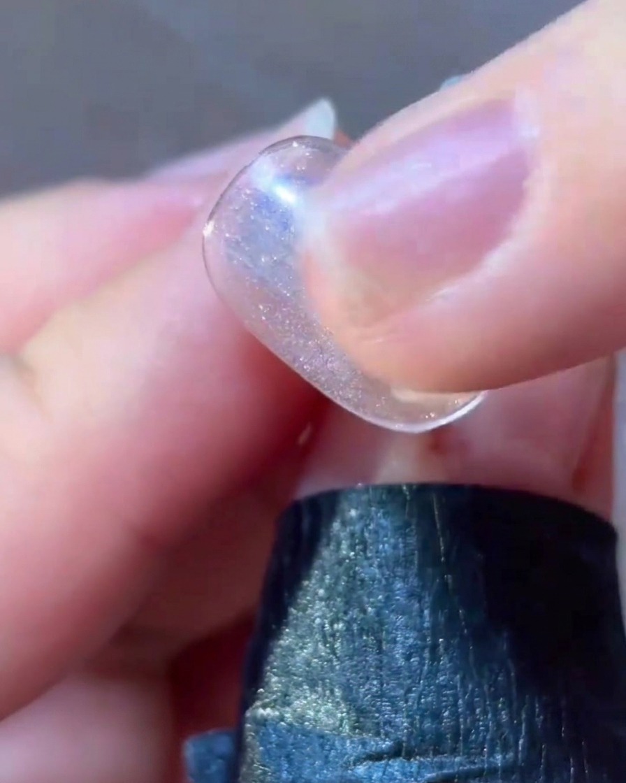 Un pincel delineador fino aplicando detalles en gel rosa alrededor del diseño de una estrella en una uña.