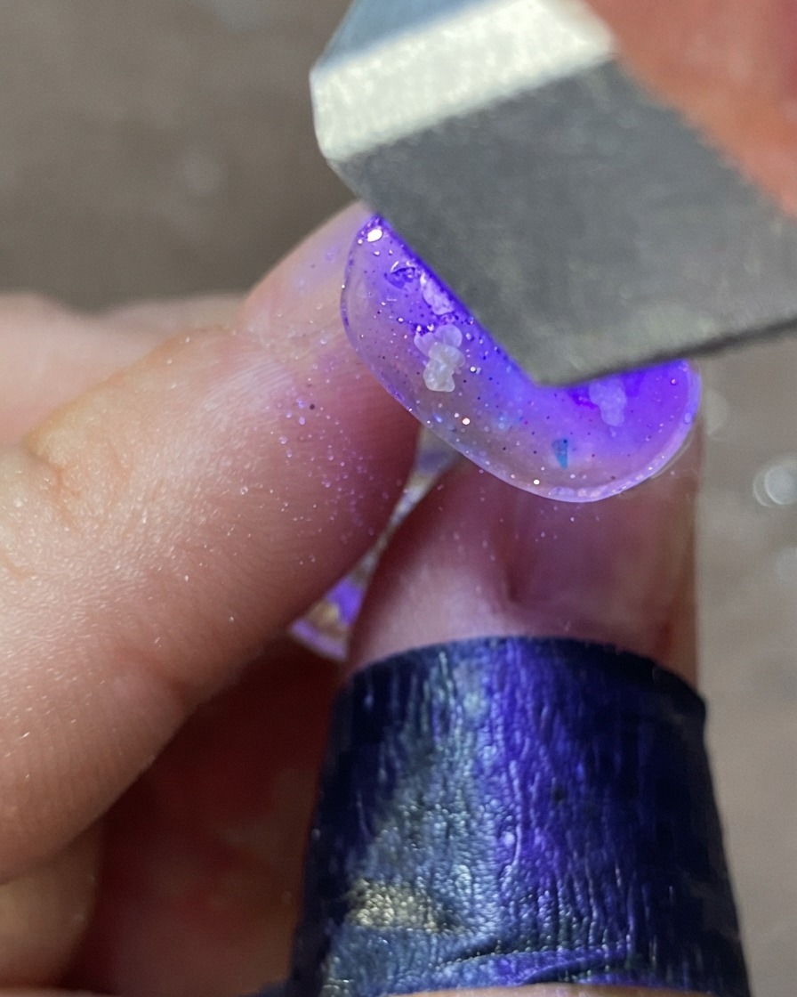Una mano colocada bajo una lámpara de uñas UV/LED morada curando un diseño de uña decorada.