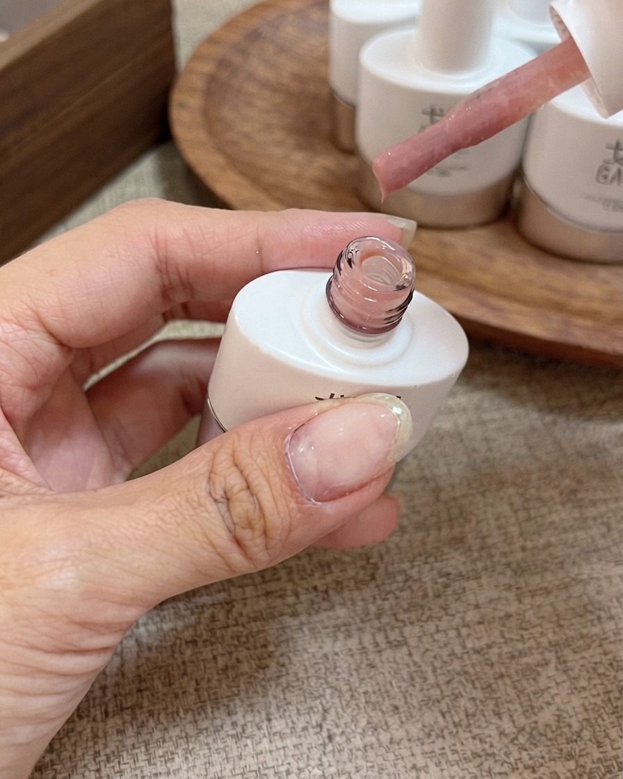 Un pincel aplicador con esmalte en gel nude rosa melocotón sostenido sobre un frasco abierto.