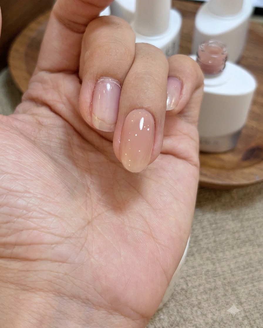 Una vista de cerca de una mano con una capa húmeda y brillante de gel base transparente aplicada sobre la uña rosa nude.
