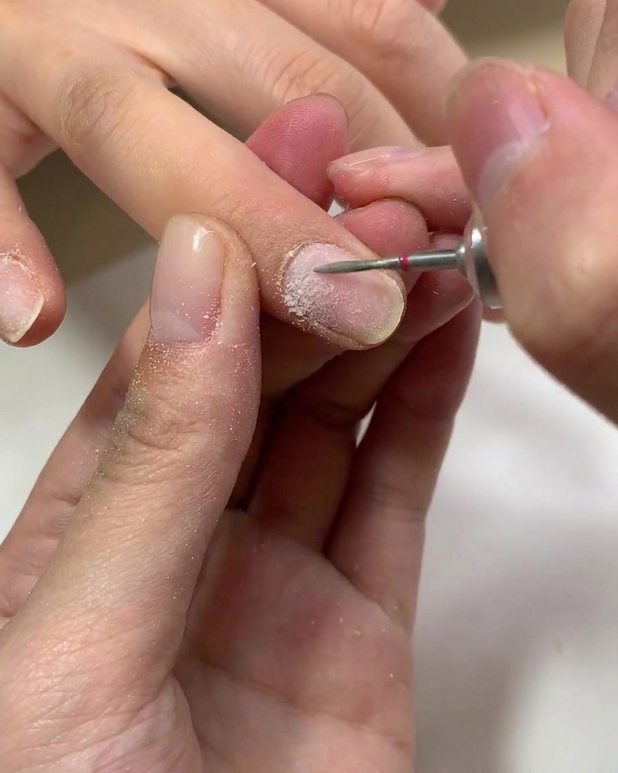Un pincel aplicando una capa transparente de base de gel sobre una uña natural.