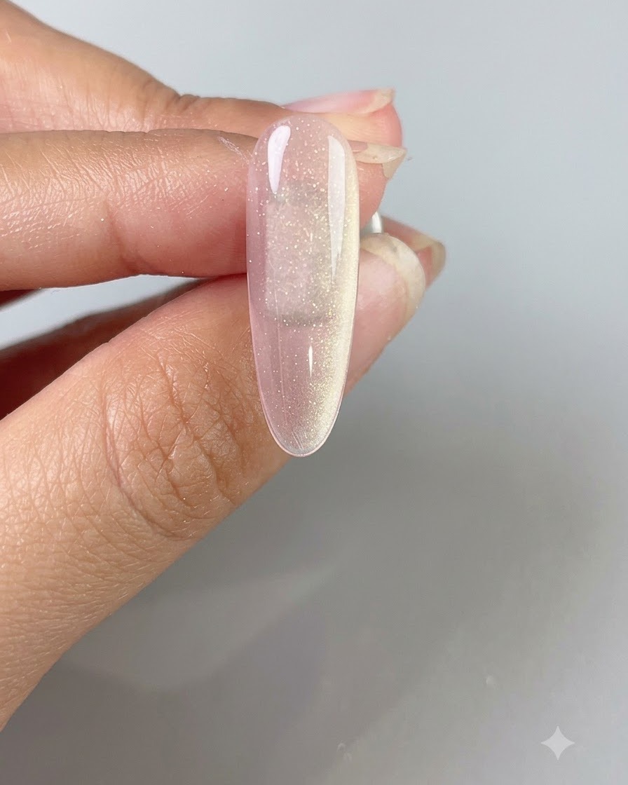 Una mano sosteniendo una varita magnética sobre una uña de gel cat-eye translúcido rosa para crear un haz de luz amplio y brillante.