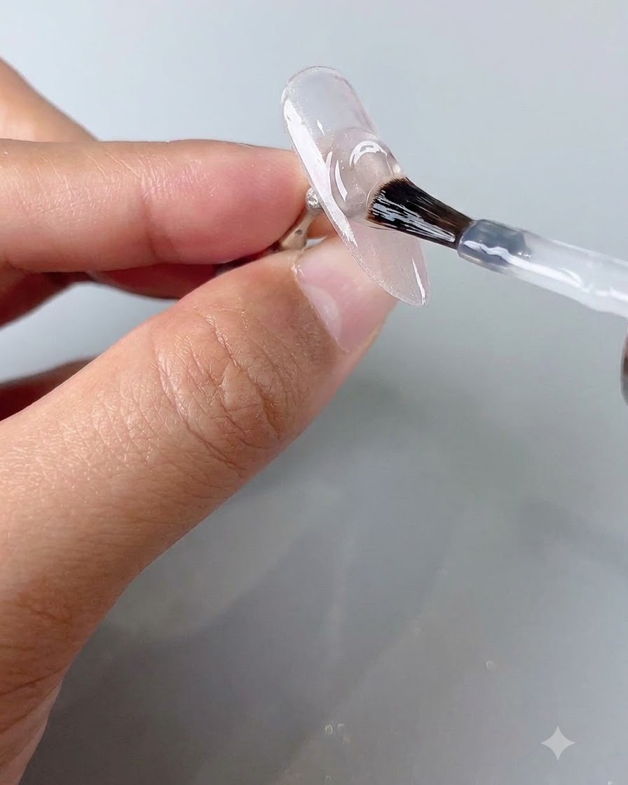 Un pincel de uñas aplicando una capa de esmalte protector transparente sobre una uña cat-eye curada.