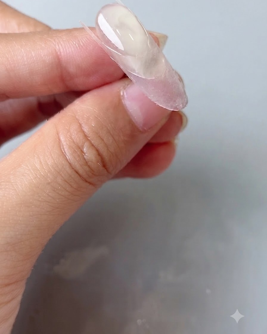 Una herramienta de silicona para uñas presionando una pegatina guía transparente en una uña ovalada.
