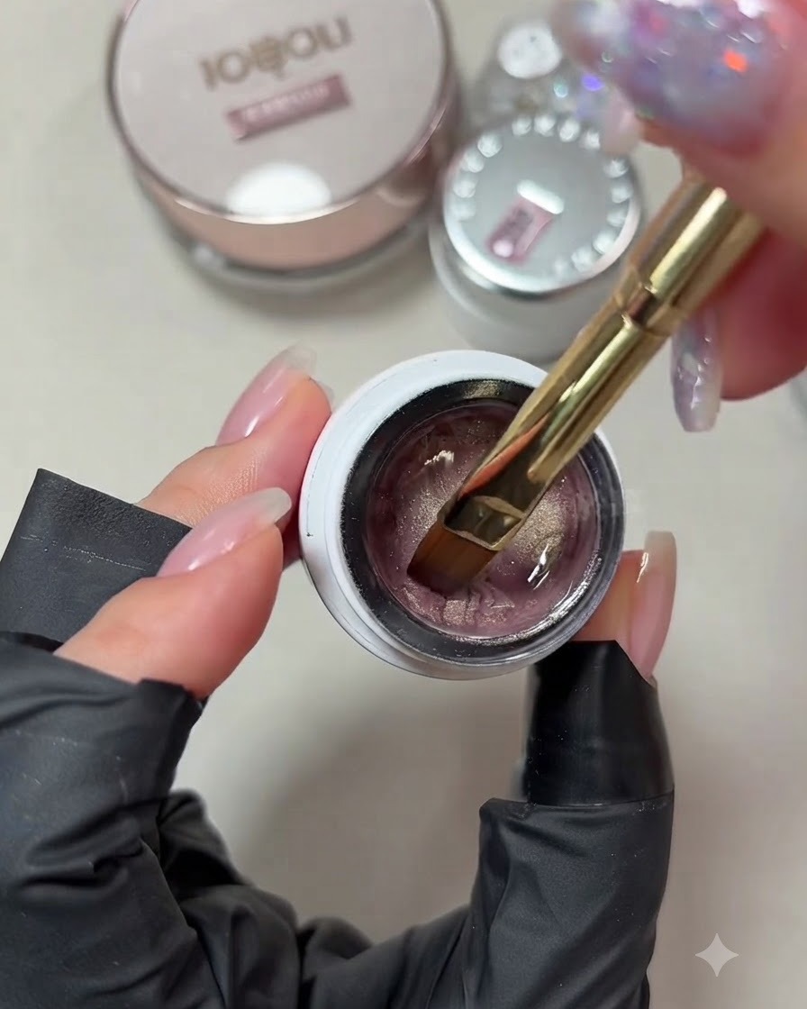 Primer plano de un pincel para gel sumergiéndose en un frasco de esmalte gel ojo de gato en tono rosa champán pálido.