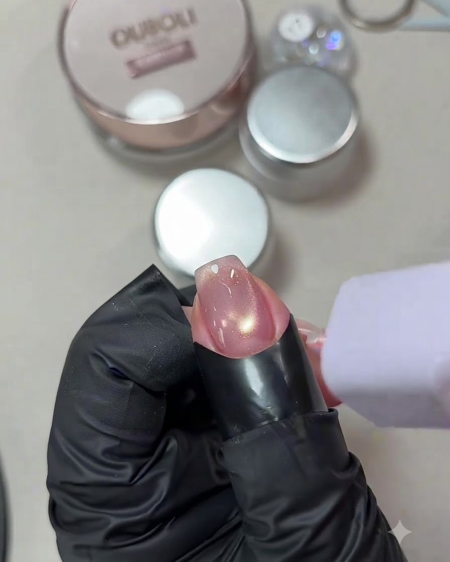 Uña con un brillante diseño de gel ojo de gato siendo curada bajo una pequeña lámpara UV/LED morada portátil.