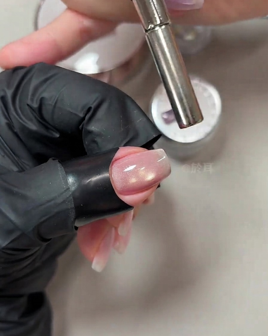 Varilla magnética cilíndrica sostenida cerca de la punta de una uña recién pintada para manipular el brillo del ojo de gato.