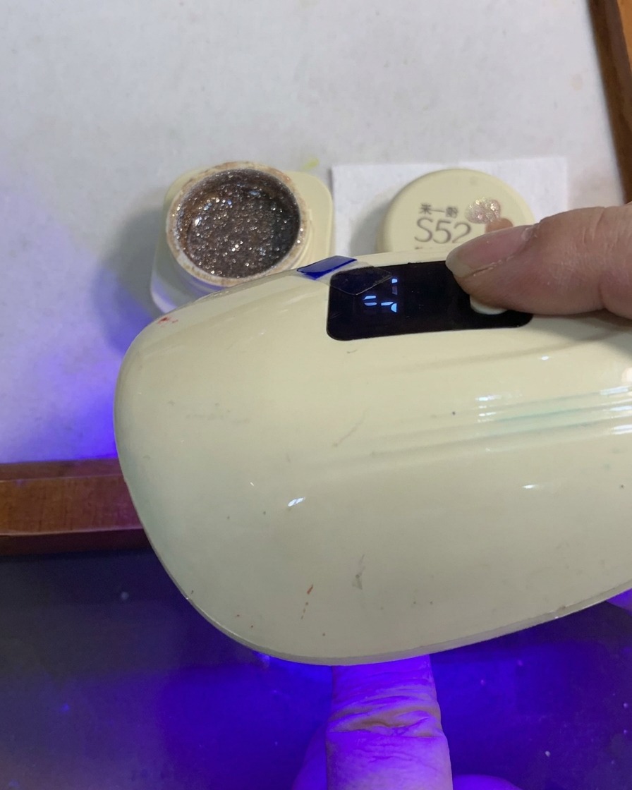 Un dedo con una uña de degradado de purpurina curándose bajo una pequeña lámpara portátil de uñas UV/LED.