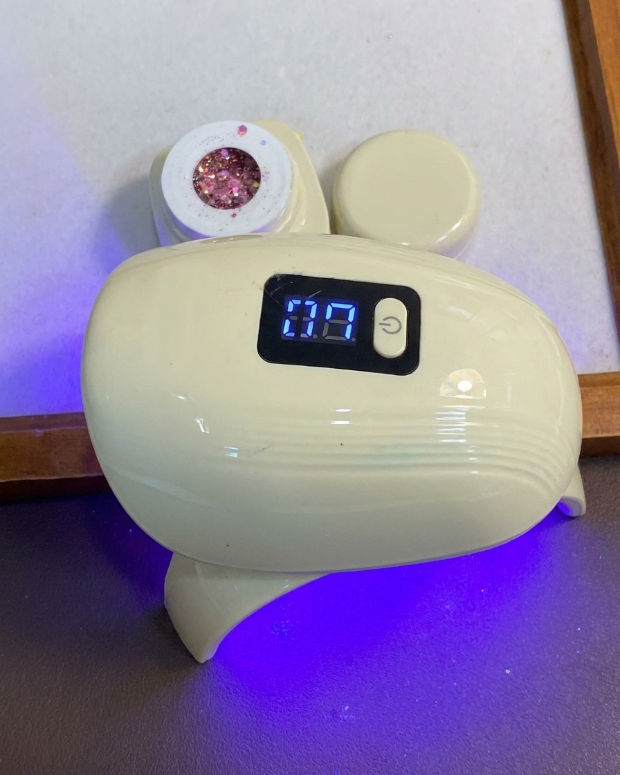 Una mano colocando los dedos bajo una lámpara compacta de curado de uñas LED azul y blanca.