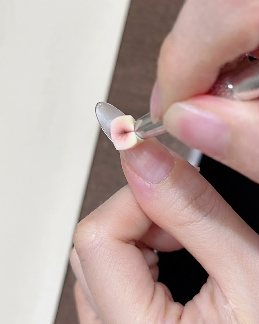 Primer plano de una pequeña esponja aplicando gel corrector nude sobre la uña natural cerca de la línea de la sonrisa.