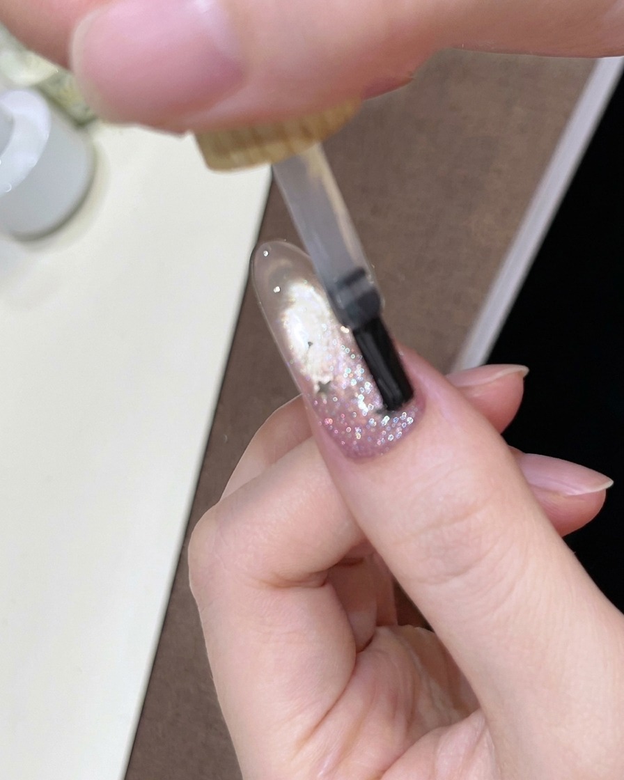 Un pincel aplicando un top coat transparente y brillante sobre la uña decorada con el degradado.