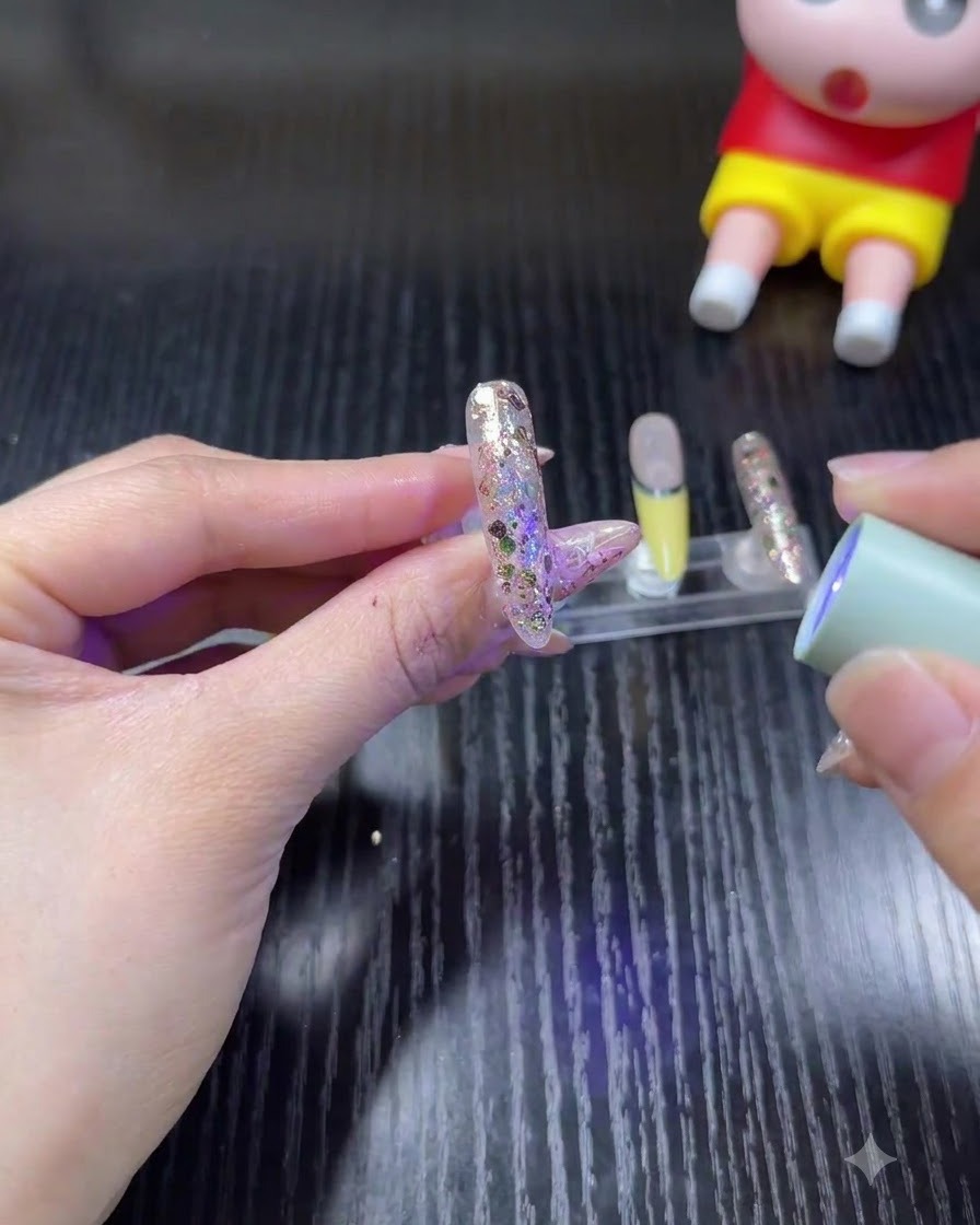 Una mano sosteniendo una minilámpara UV/LED portátil sobre una uña brillante para curar el gel.