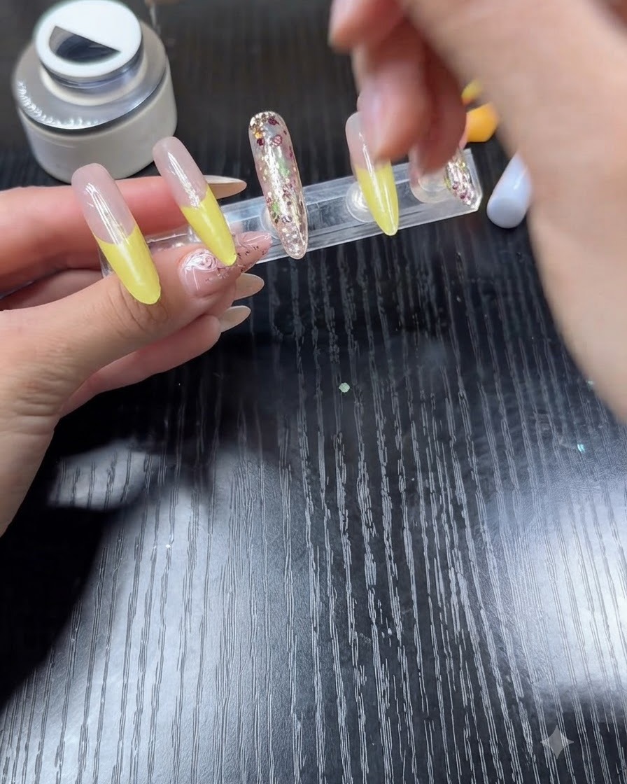 Un pincel de esmalte de uñas aplicando capa superior transparente sobre una uña con punta francesa de color amarillo brillante.