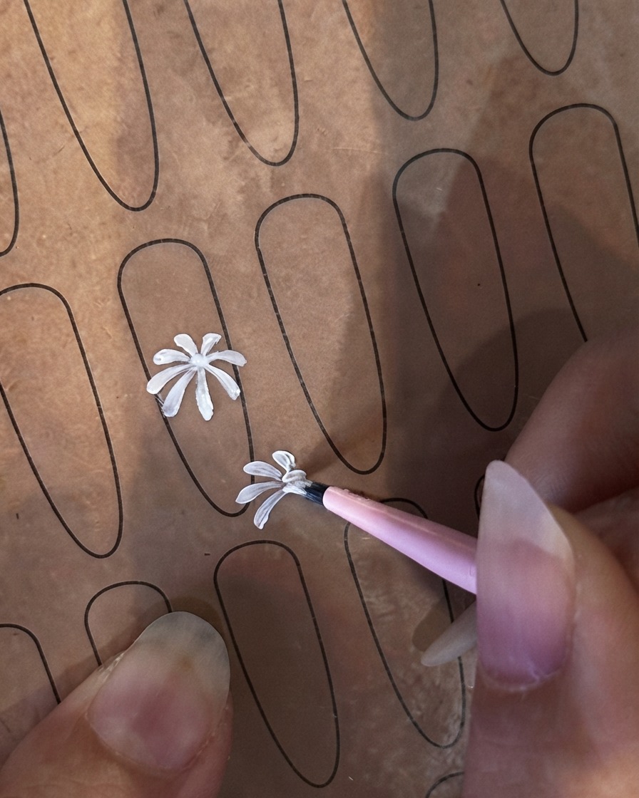 Un pincel delineador fino comenzando un segundo pétalo blanco más pequeño en una plantilla de práctica de uñas.