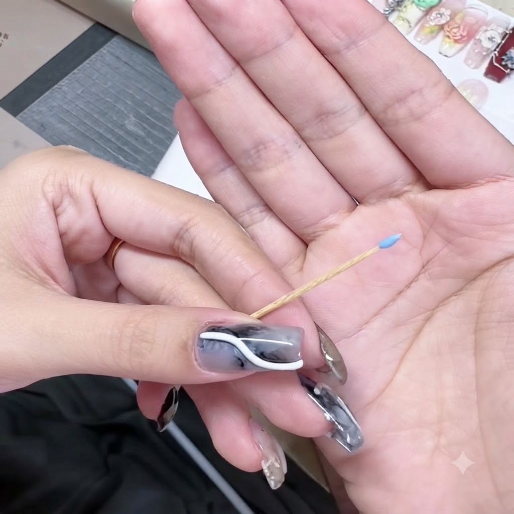 Un palillo sostenido en una mano con una pequeña perla de gel azul en su punta afilada.