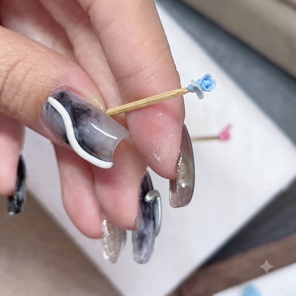 Un pequeño capullo de rosa azul en un palillo sostenido entre los dedos, mostrando la colocación de un nuevo pétalo.