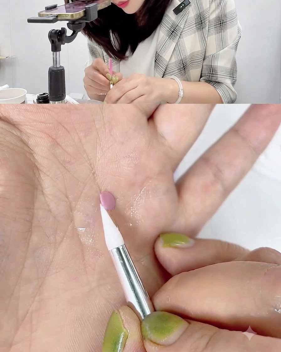 Un pincel de silicona blanco tocando y enrollando el borde de un pequeño disco de gel rosa sobre la palma de una mano.
