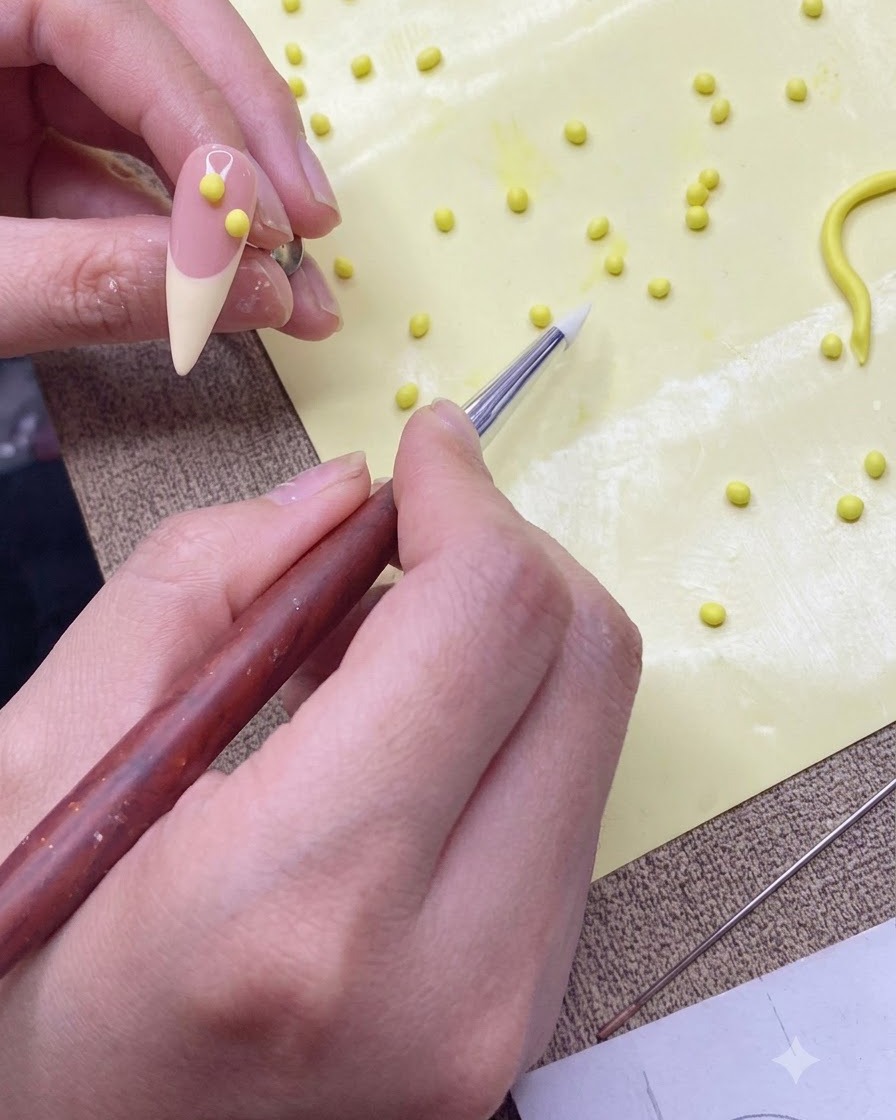 Un lápiz moldeador de silicona transfiriendo una pequeña bola de gel amarillo a un tip de práctica de color nude.
