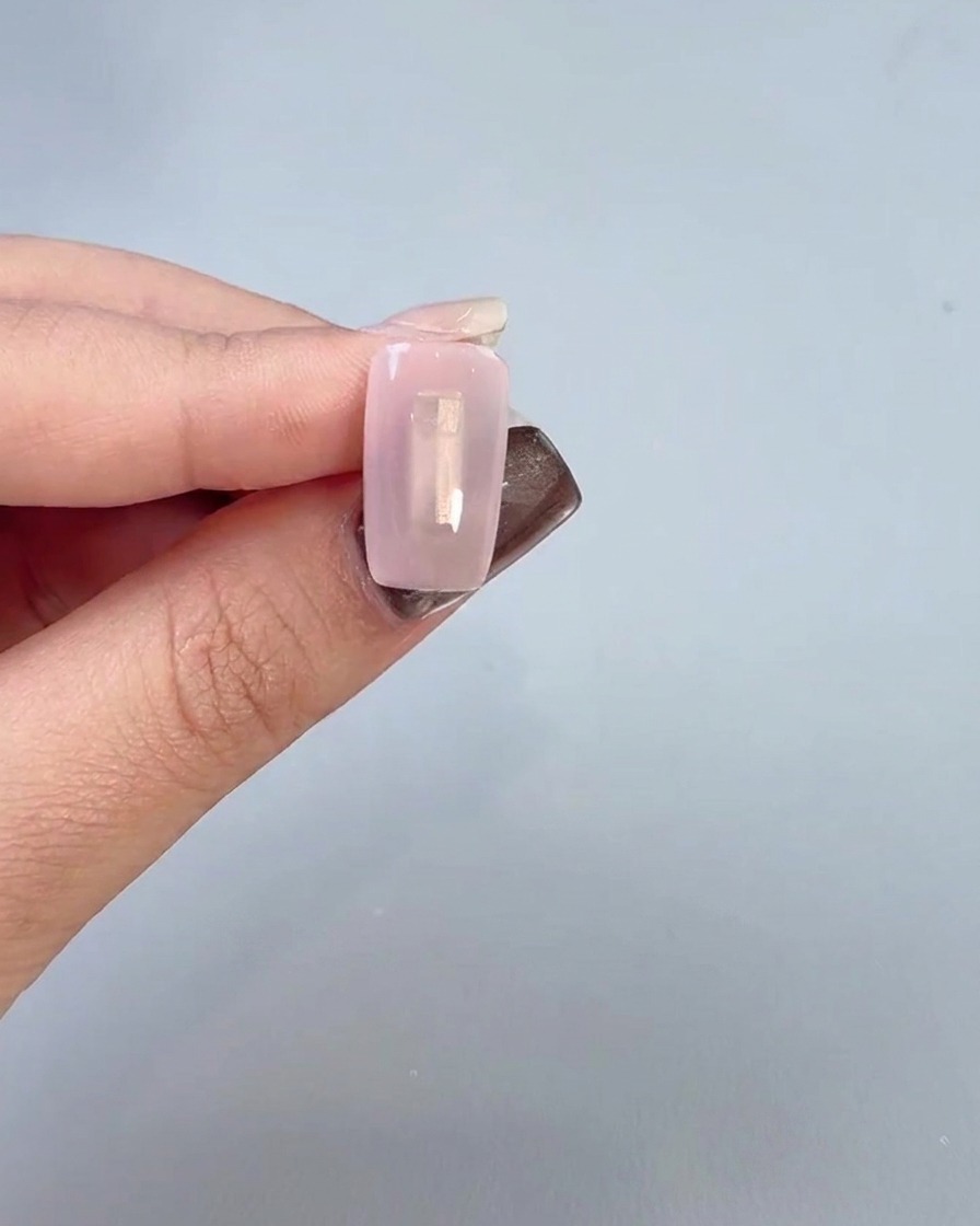 Primer plano de una mano aplicando una capa base transparente de gel sobre la superficie de la uña con un pincel.