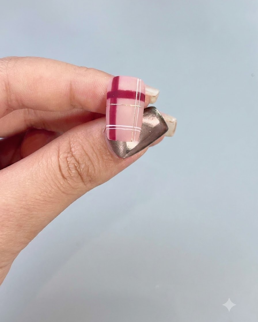 Primer plano de una uña decorada que presenta un patrón a cuadros rojo y blanco con toques dorados.