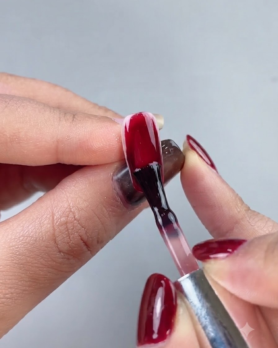 Un pincel de uñas aplicando un esmalte en gel rojo sangre de buey profundo sobre una extensión de uña completa.